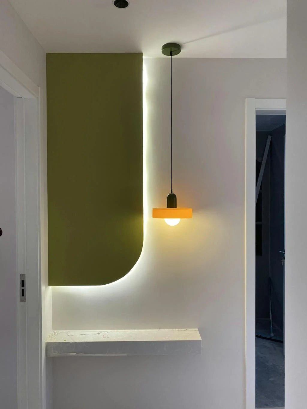 Modern interior design with a green wall, white shelf, and pendant light.