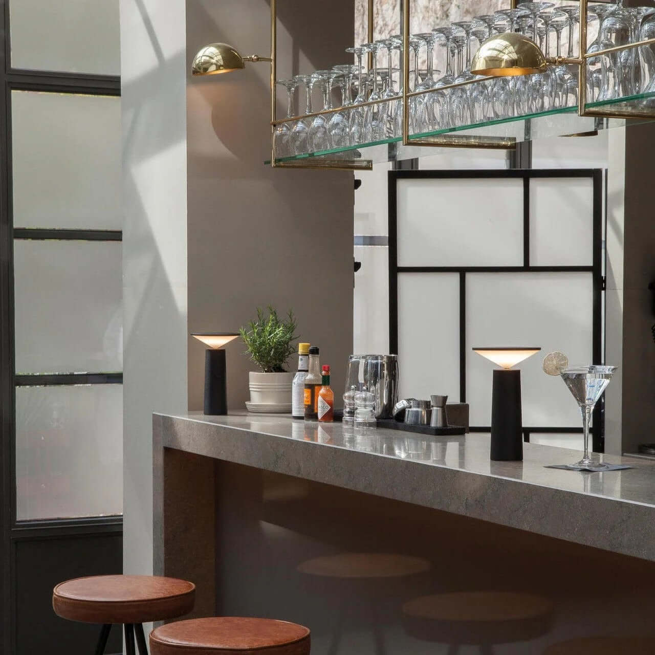 Rivo cordless table lamp illuminating a modern kitchen bar with stylish decor and glassware accents.