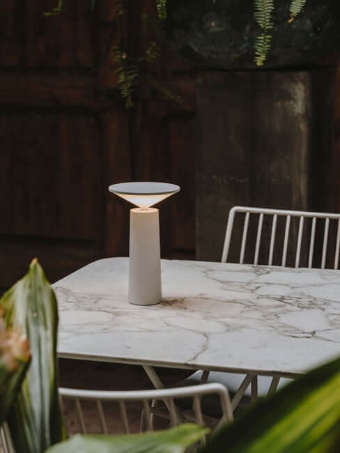 Rivo cordless table lamp on a marble table surrounded by greenery, providing warm, ambient light.
