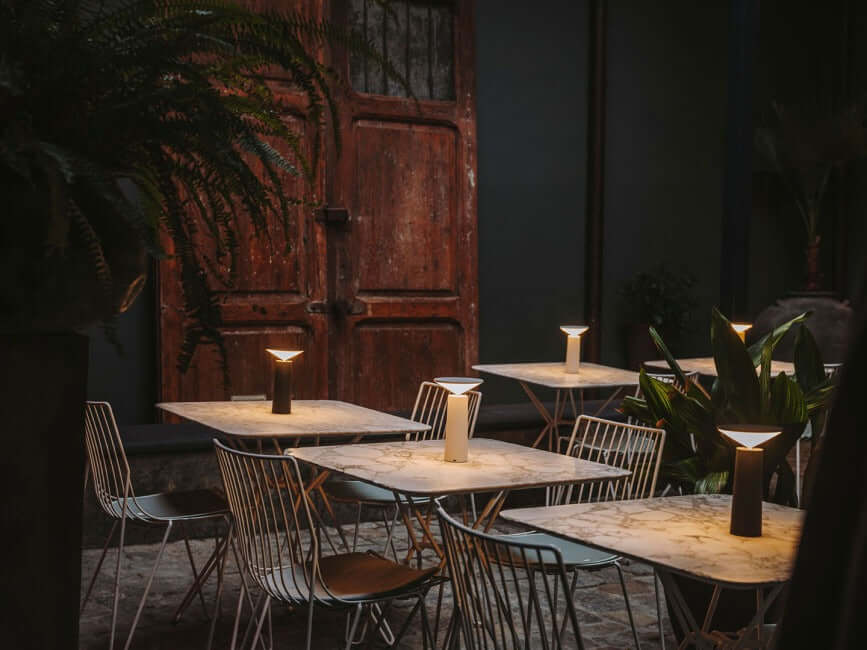 Rivo cordless table lamp on outdoor dining tables, providing modern ambient light in a stylish setting.