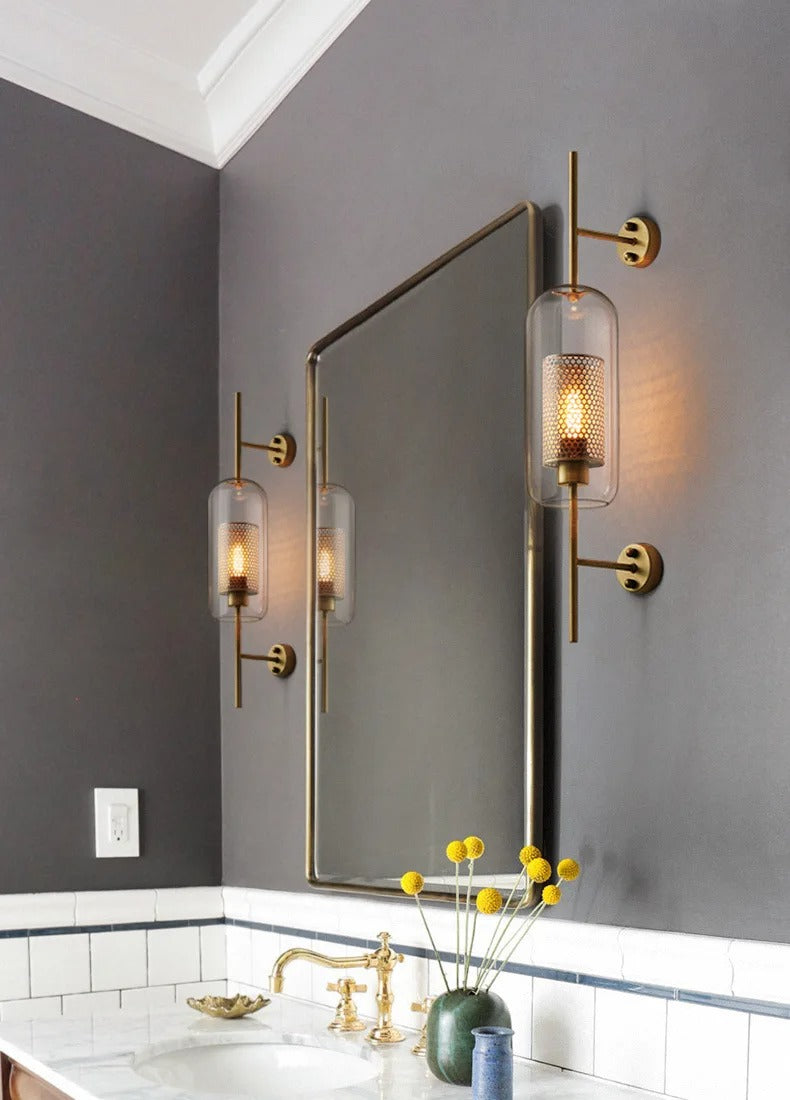Bathroom with a mirror, gold fixtures, and wall lights on a gray wall.