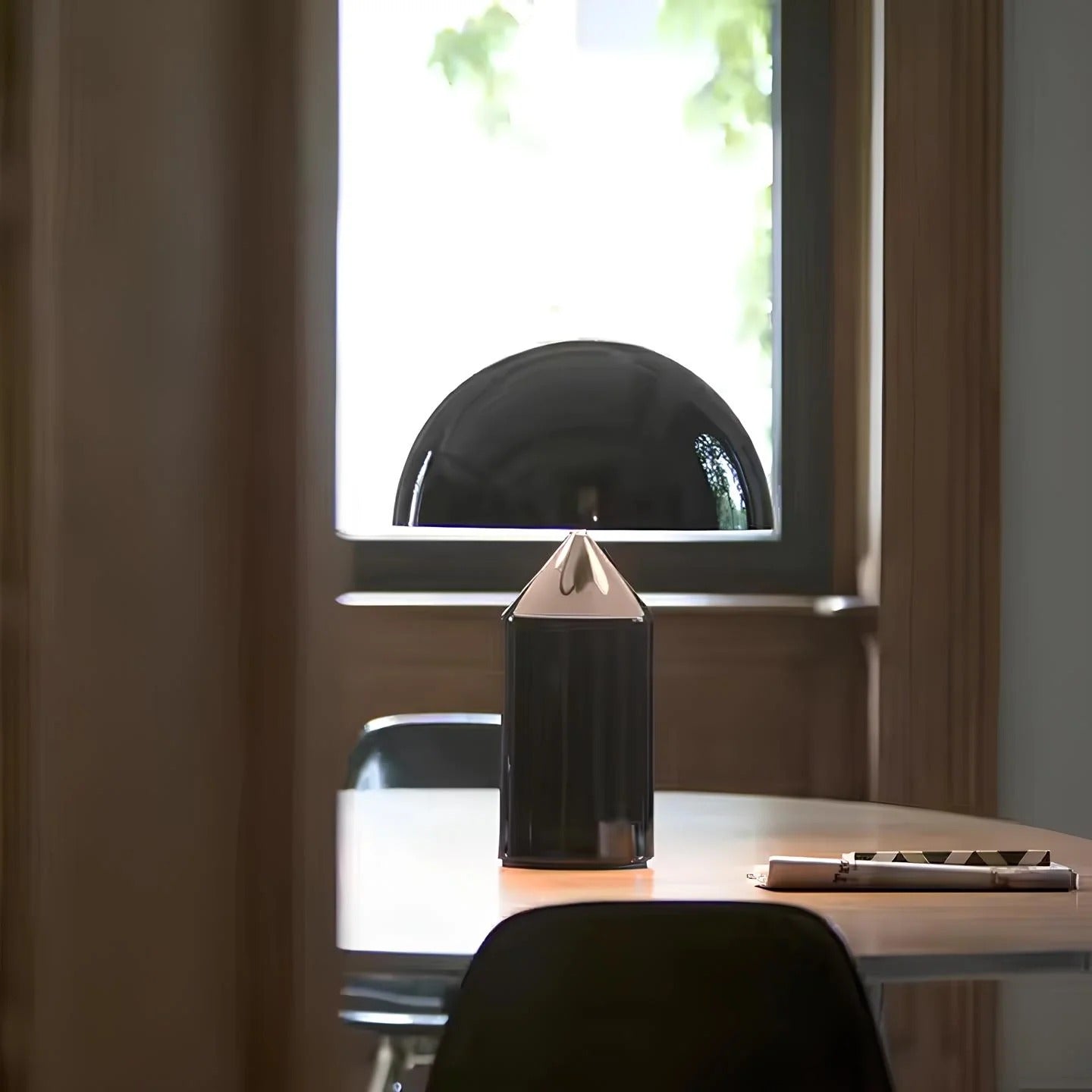 Black geometric lamp on a desk with a window in the background