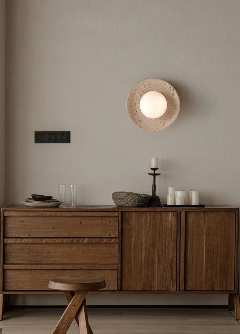 Wooden sideboard with decorative items against a beige wall with a round wall light fixture.