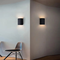 Two black wall lights on a white wall with a chair in the foreground.