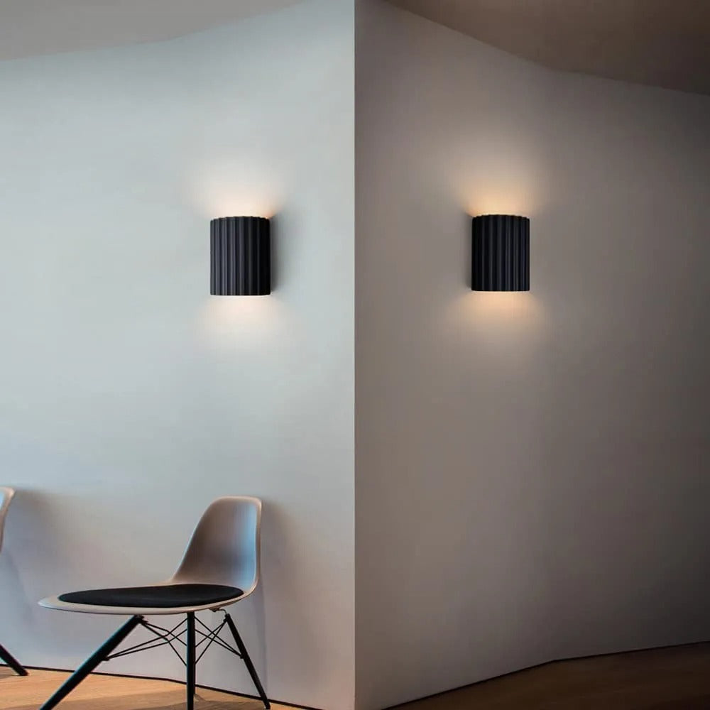 Two black wall lights on a white wall with a chair in the foreground.