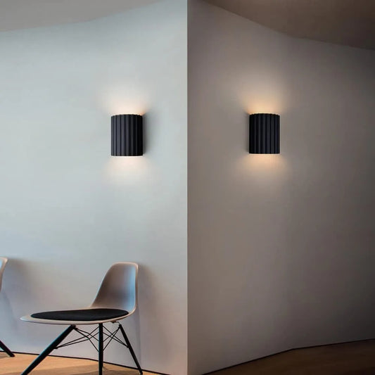 Two black wall lights on a white wall with a chair in the foreground.