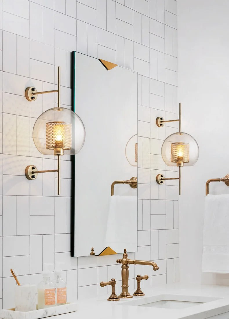 Bathroom with gold fixtures, including wall sconces and faucet, against a tiled wall.