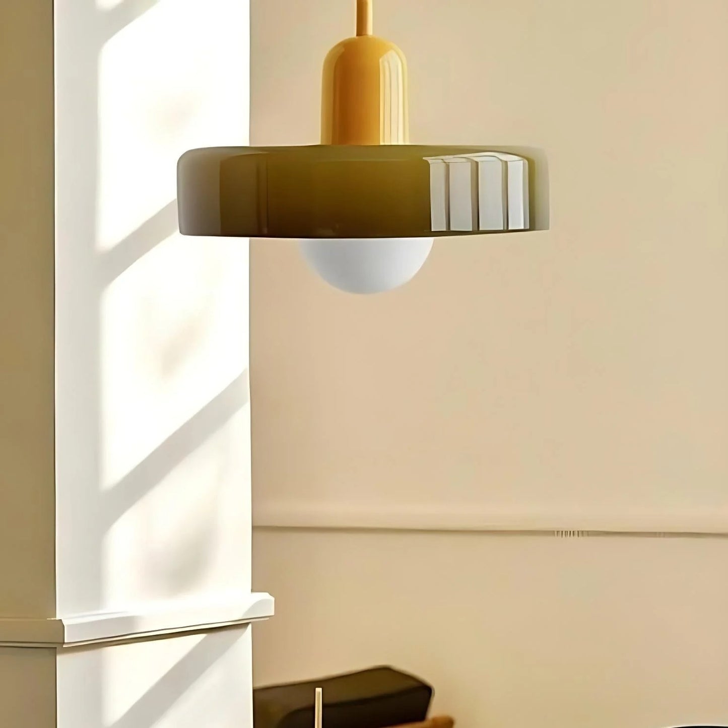 Modern pendant light with a gold fixture and greenish-brown shade hanging in a room.