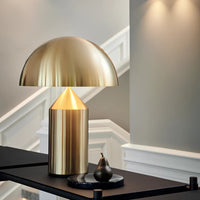 Gold table lamp on a dark surface with a pear in a room setting.