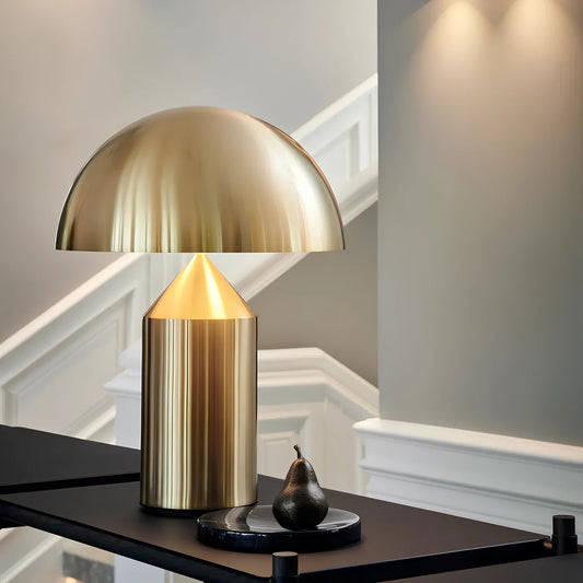 Gold table lamp on a dark surface with a pear in a room setting.