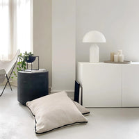 Modern interior with a white floor lamp, black cylindrical side table, and white floor pillow.