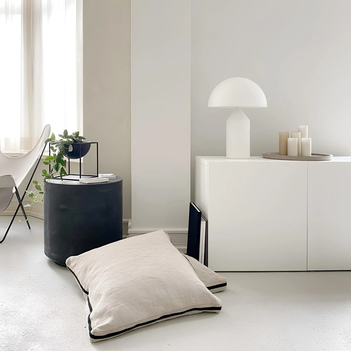 Modern interior with a white floor lamp, black cylindrical side table, and white floor pillow.