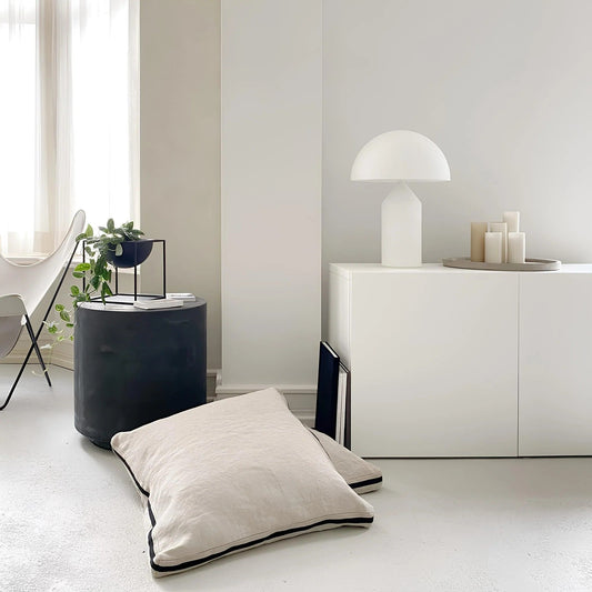 Modern interior with a white floor lamp, black cylindrical side table, and white floor pillow.
