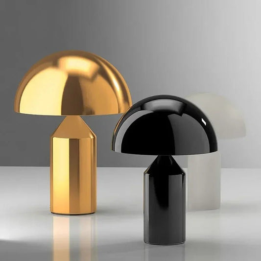 Two table lamps, one gold and one black, on a reflective surface with a neutral background.