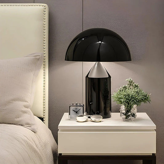Black table lamp on a white nightstand next to a bed with gray walls.