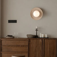 Wooden sideboard with decorative items against a beige wall with a round wall light fixture.