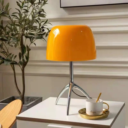 Orange table lamp on a white surface with a cup and plant in the background