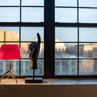 Red lamp and black sculpture on a windowsill with cityscape view