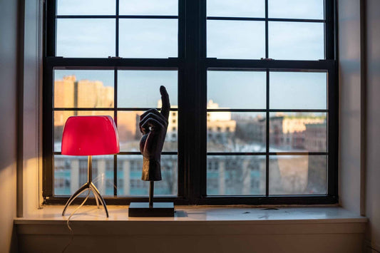 Red lamp and black sculpture on a windowsill with cityscape view